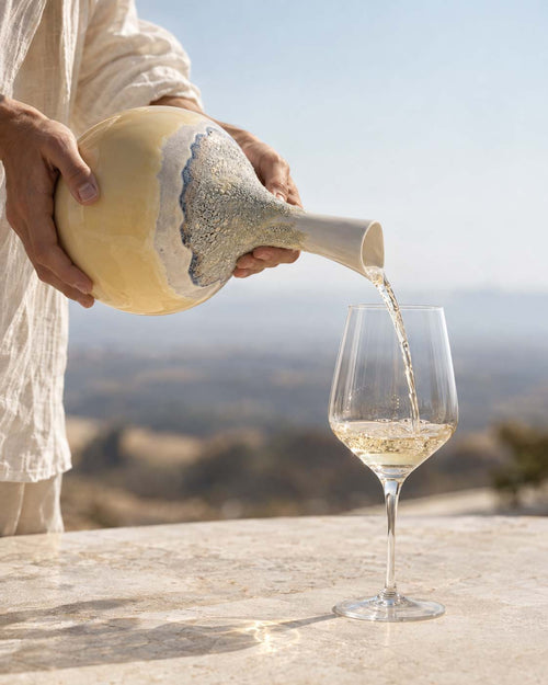 Pouring ZEN Chardonnay from the CALASSI vessel into a glass on a terrace above the hills
